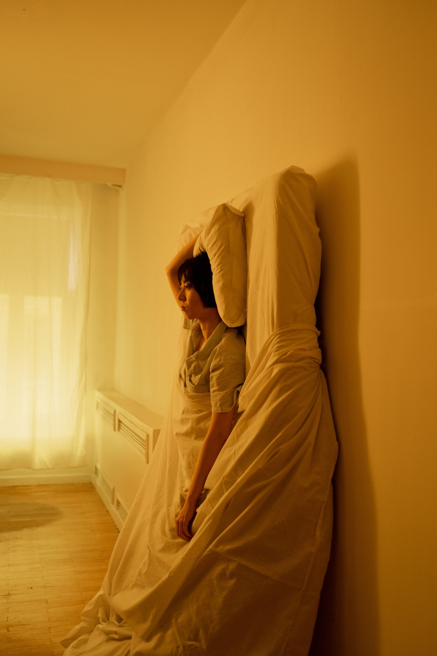 trouble du sommeil vigilance Femme assise éveillée contre son matelas redressé à la verticale, illustrant la vigilance nocturne et les troubles du sommeil.
