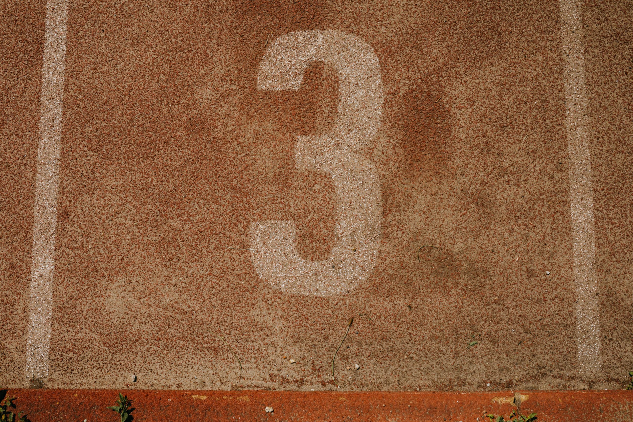 Close-up of a textured running track with the number three, showcasing sport simplicity and earthy tones.